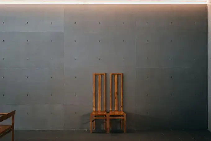 Temsilî görsel, brüt beton görünümlü panel duvar ve önünde ahşap sandalye