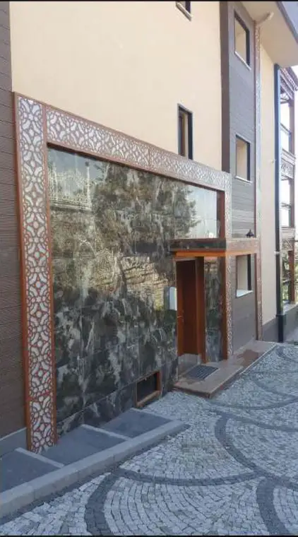 Villa Başdemir cephe detayı, delikli dekoratif panel, mermer görünümlü kaplama ve ahşap çerçeveli cam kapı